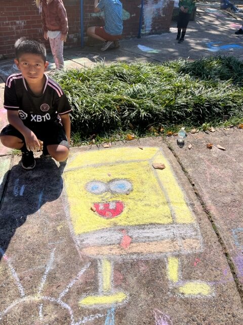 A student sits near a chalk art drawing of Spongebob Squarepants