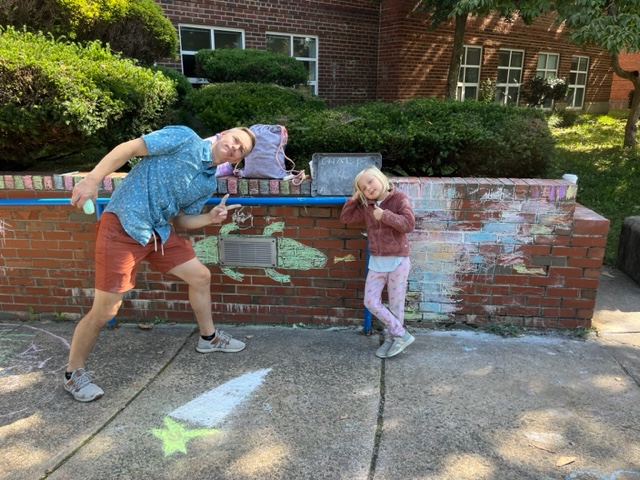 A family stands near a chalk art drawing of a lizard.