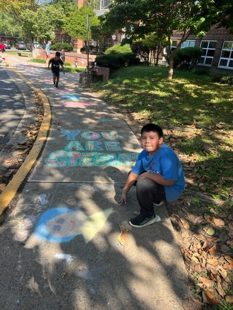 A student sits near a chalk art drawing.