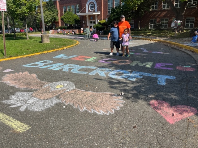 a family stands near chalk art on the Barcroft bus loop that reads "Welcome to Barcroft"